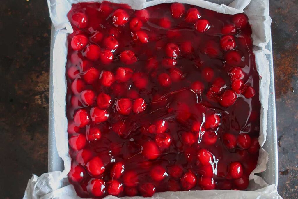cherry pie filling spread over cake batter in a square pan