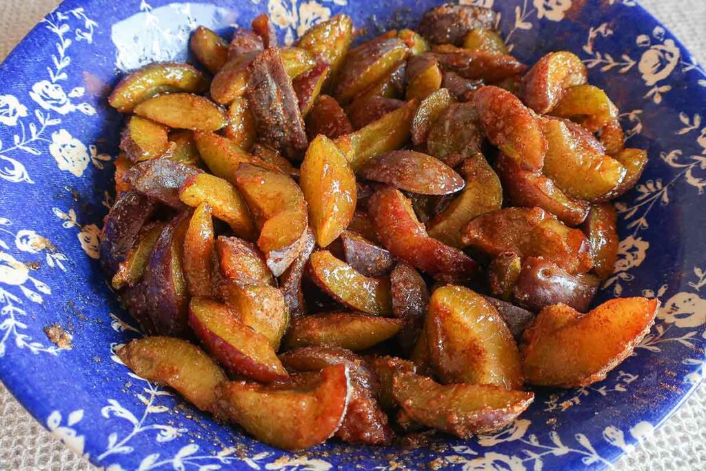 sliced plums in a bowl with cardamom and sugar
