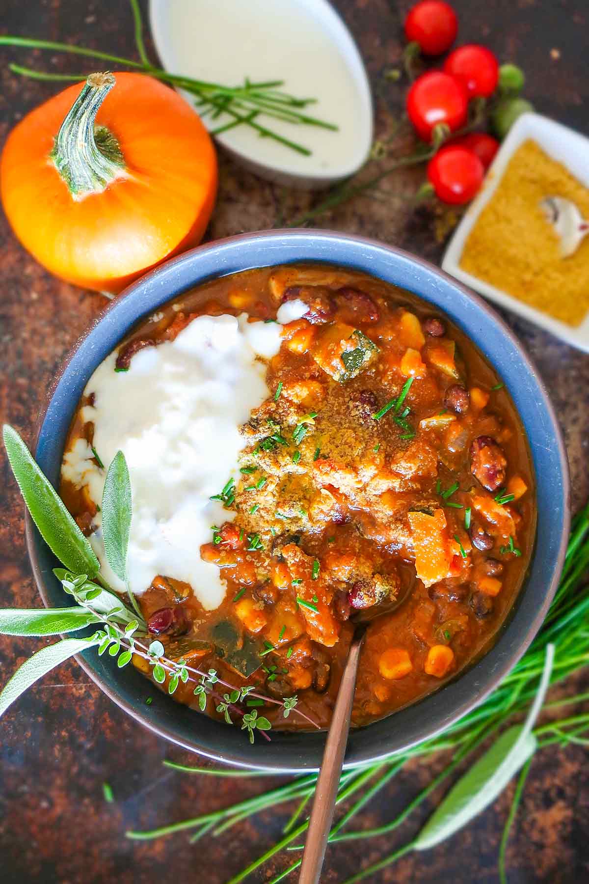vegan pumpkin chili in a bowl topped with herbs, nutritional east and vegan cream