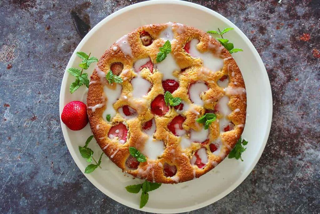 round strawberry cake with buttermilk glaze on a plate with mint garnish