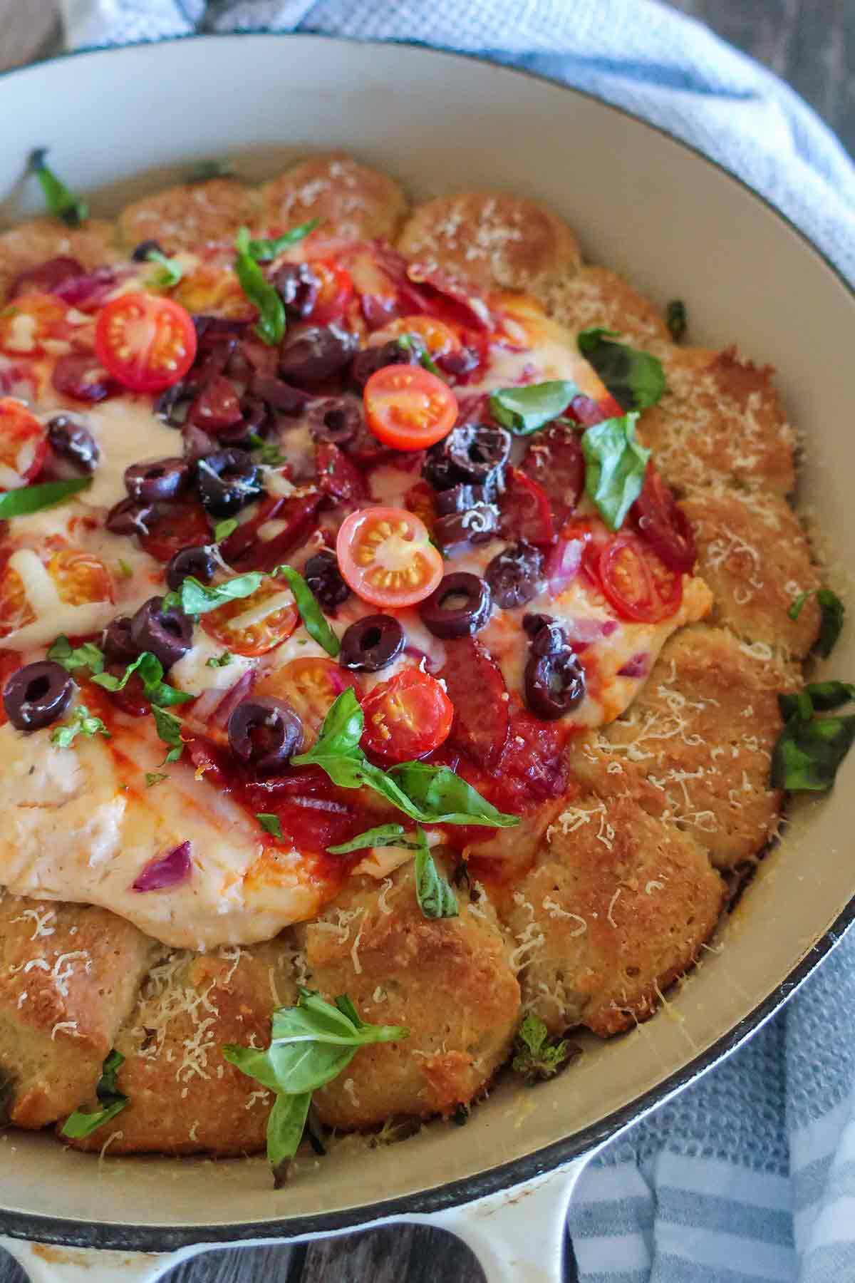 baked pizza dip with toppings and rolls in a skillet