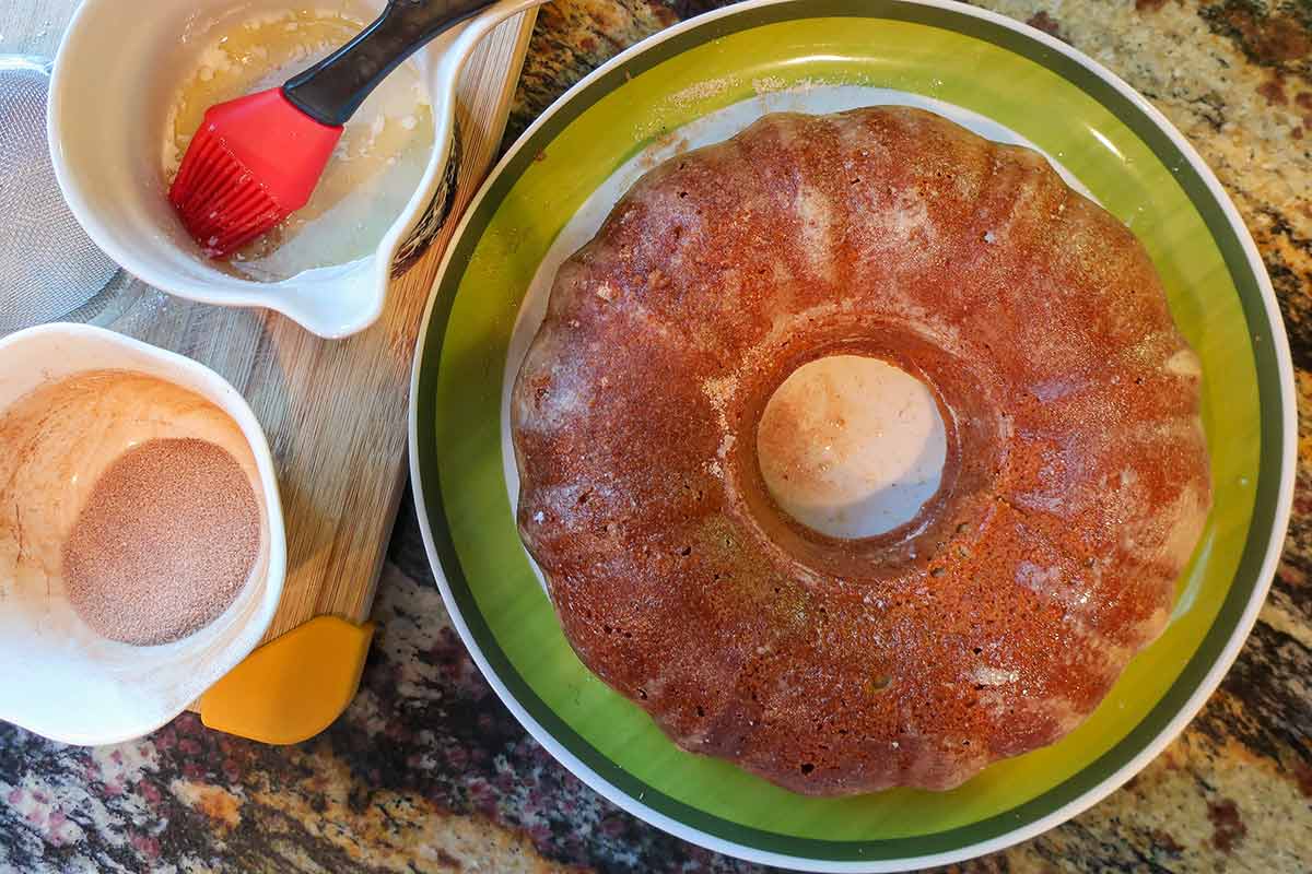 whole apple cider donut cake on a plate with melted butter and cinnamon spice on the side