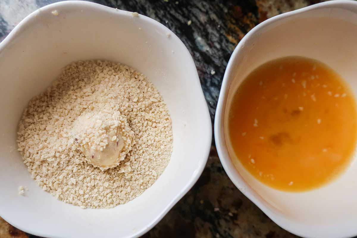 two bowls; egg wash and breadcrumbs coating a goat cheese ball