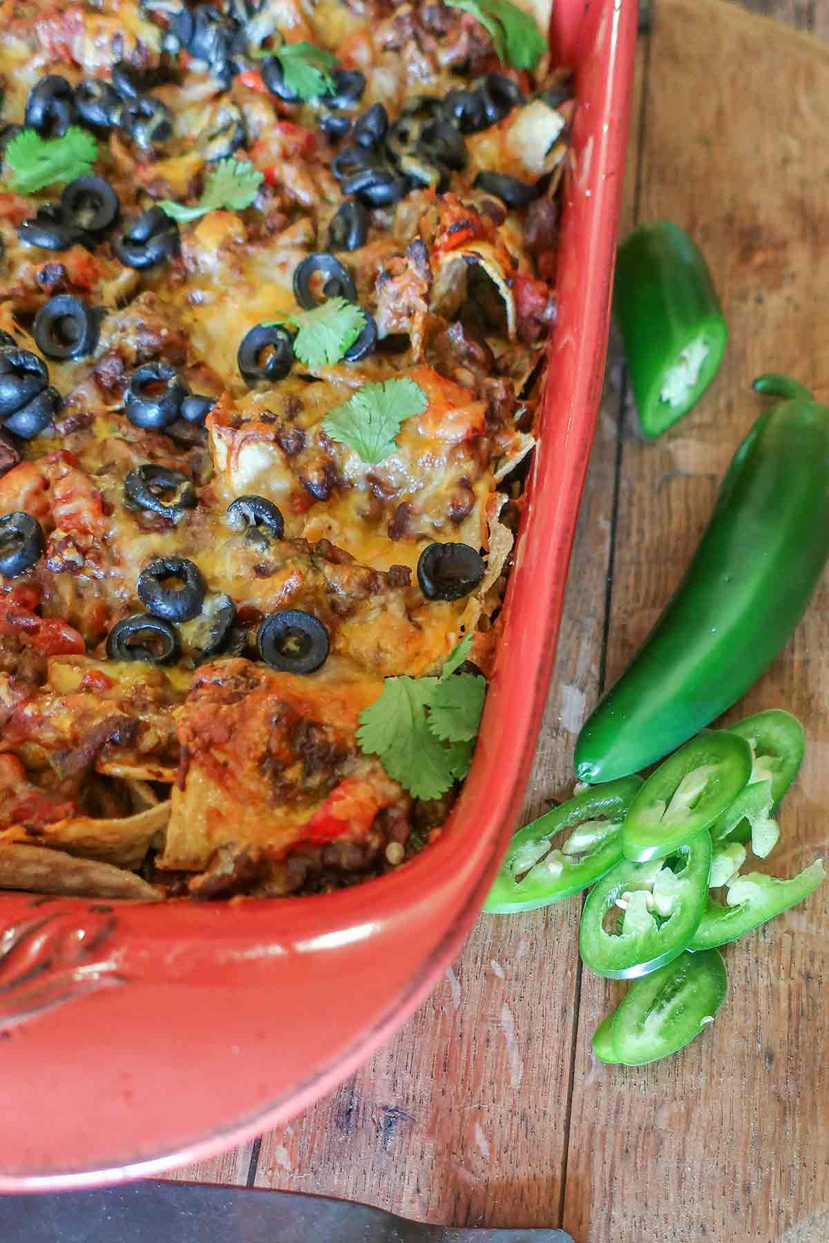 nacho casserole showing topping of melted cheese, olives, jalapenos and cilantro