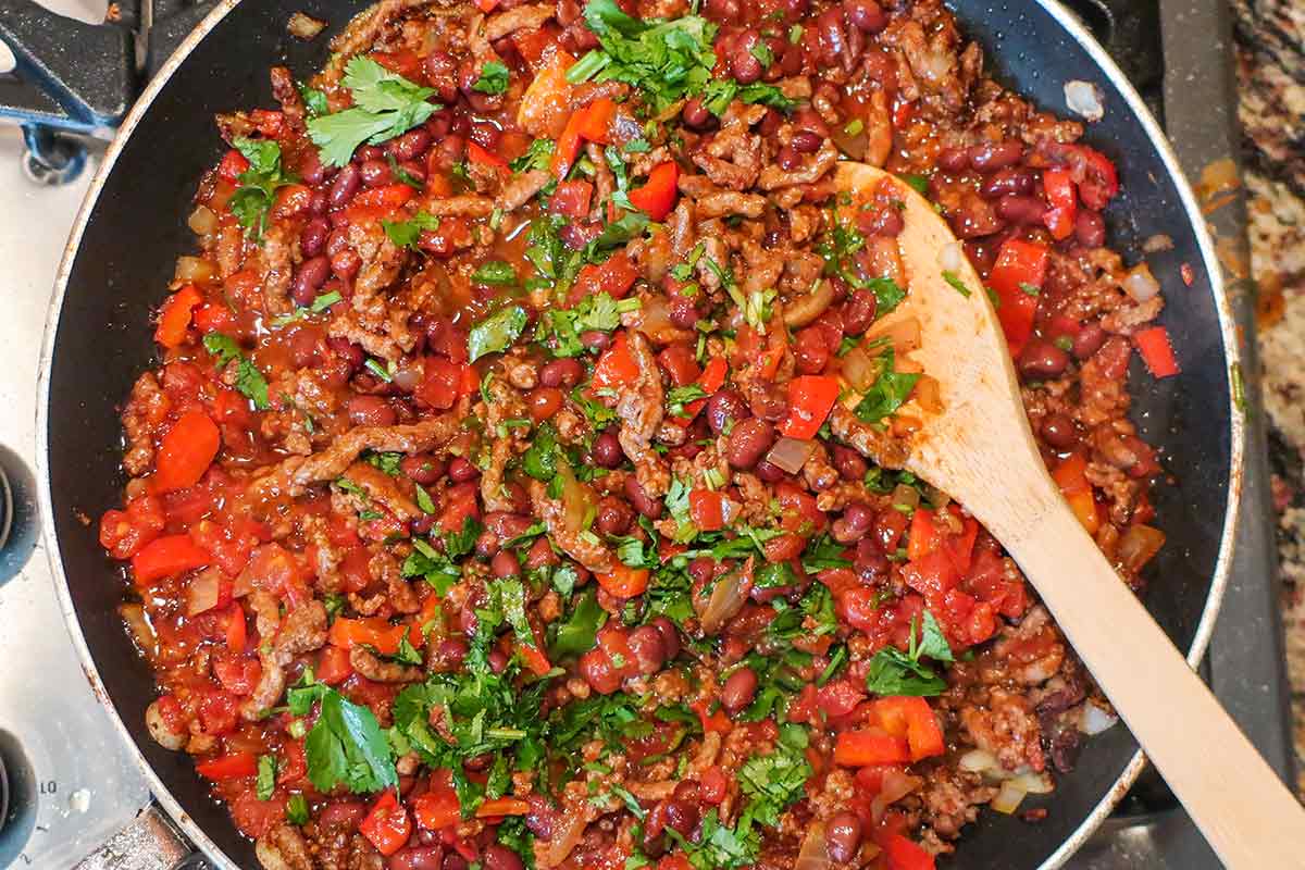 seasoned ground beef with beans, tomatoes, bell peppers, olives, onions, cilantro in a skillet