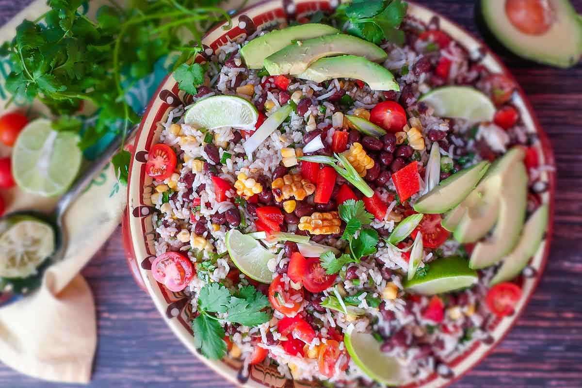 garnished black bean rice salad with avocado, lime wedges and herbs