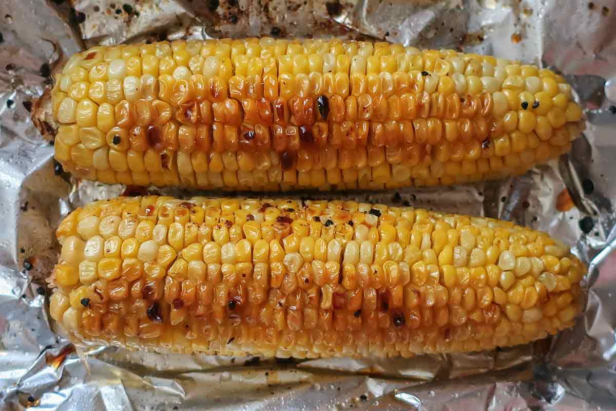two corn on the cob roasted in the oven on foil paper