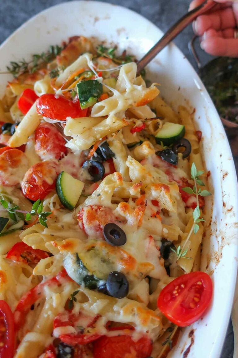 scooping out creamy cheesy pasta with veggies from a casserole dish using a spoon