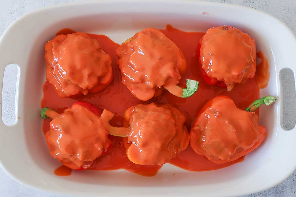 6 stuffed peppers with sauce in a dish before baking