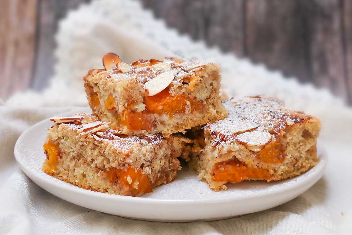 Three slices of gluten-free farmer’s apricot cake on a plate, topped with sliced almonds and a light dusting of powdered sugar