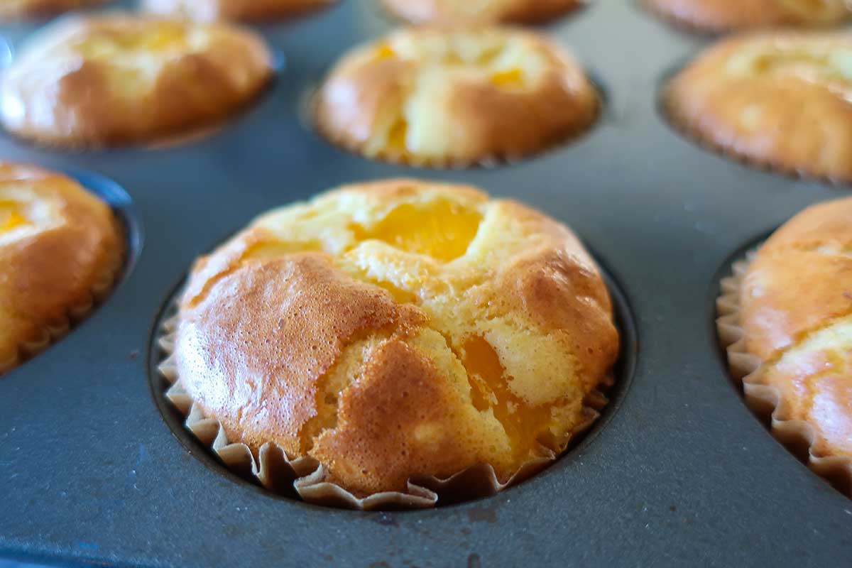 close up of baked peach pudding muffin in a muffin pan