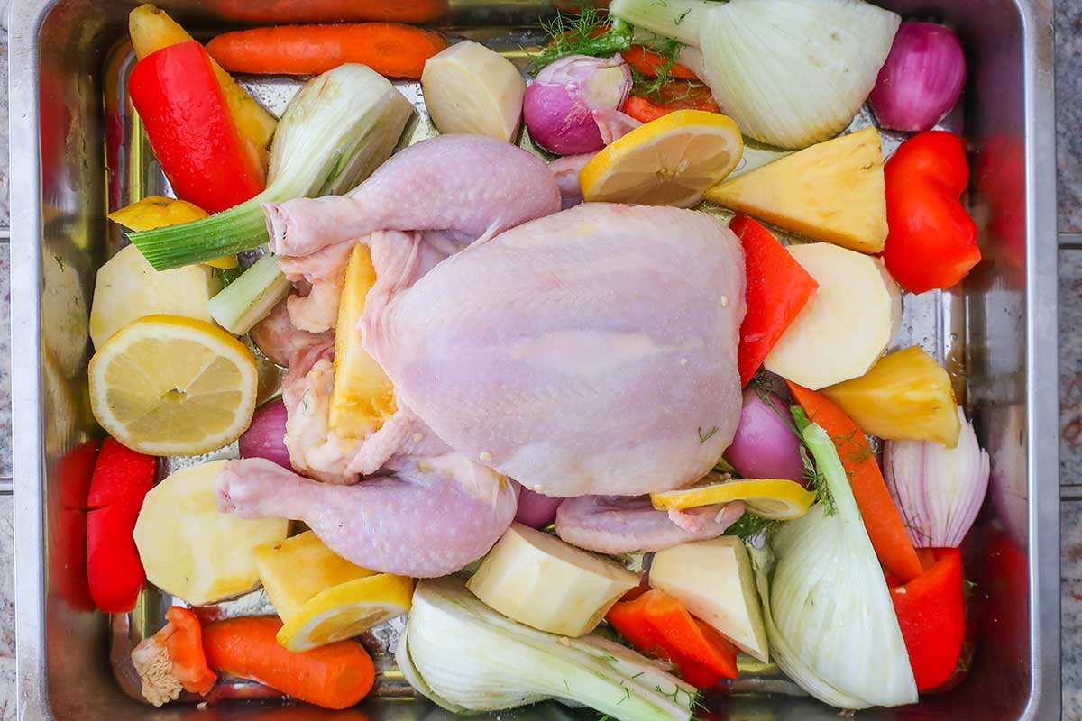 uncooked whole chicken and veggies in a roasting pan