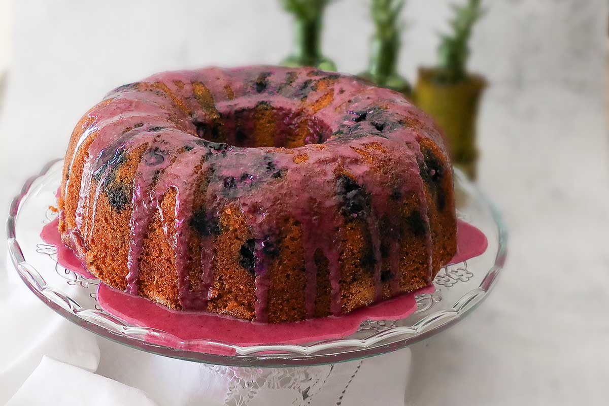 whole blueberry bundt cake on a cake platter drizzles with blueberry orange glaze
