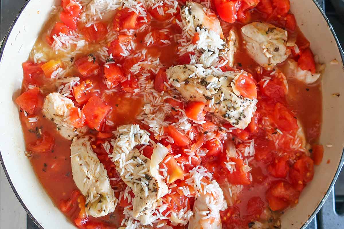 uncooked rice, chopped tomatoes, seared chicken and spices in a skillet 