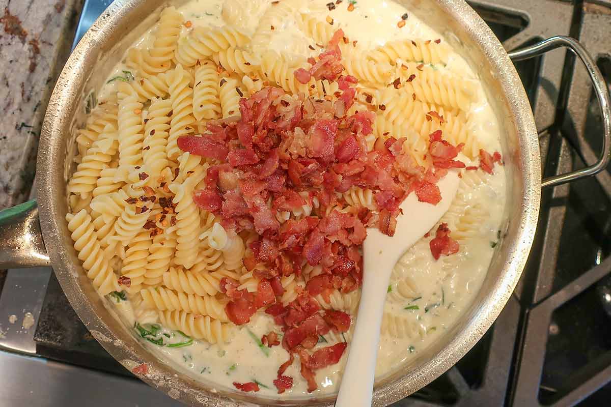 adding pasta and bacon to the spinach cream cheese sauce