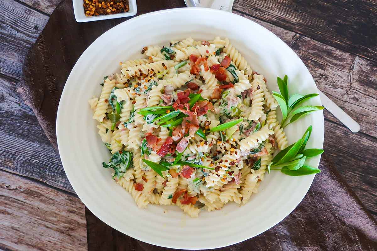 bacon and spinach cream cheese pasta on a plate with fresh herbs