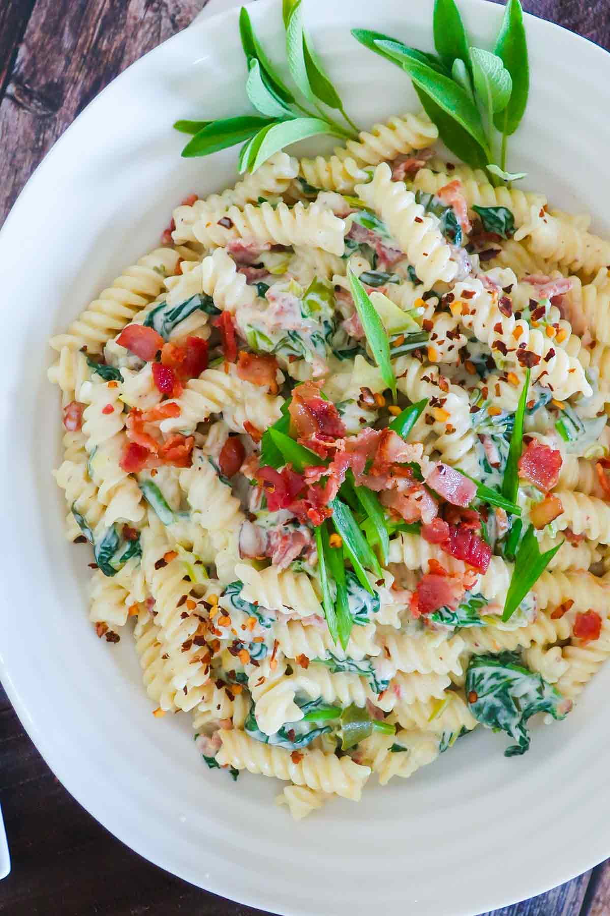 bacon and spinach cream cheese pasta dish with herbs in a large pasta bowl