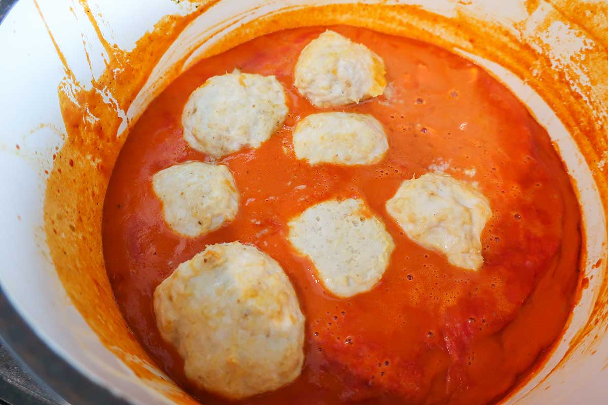 sauce topped with cooked chicken meatballs in a pot