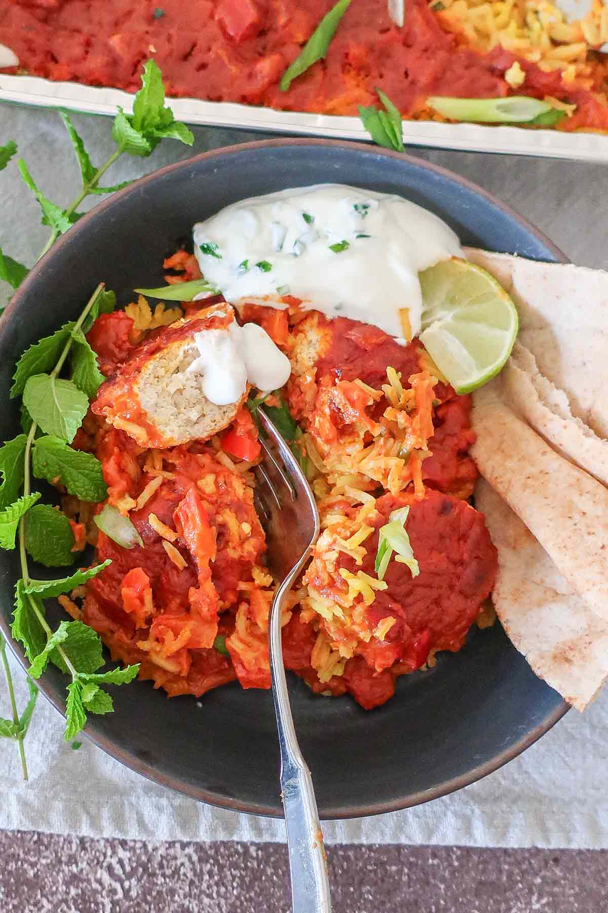 butter chicken meatballs rice casserole topped with yogurt, lime wedges and herbs