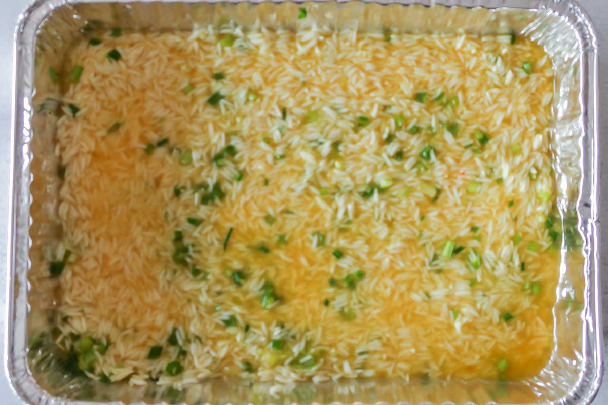 dry rice mixed with cumin, turmeric, green onions and broth in a baking dish