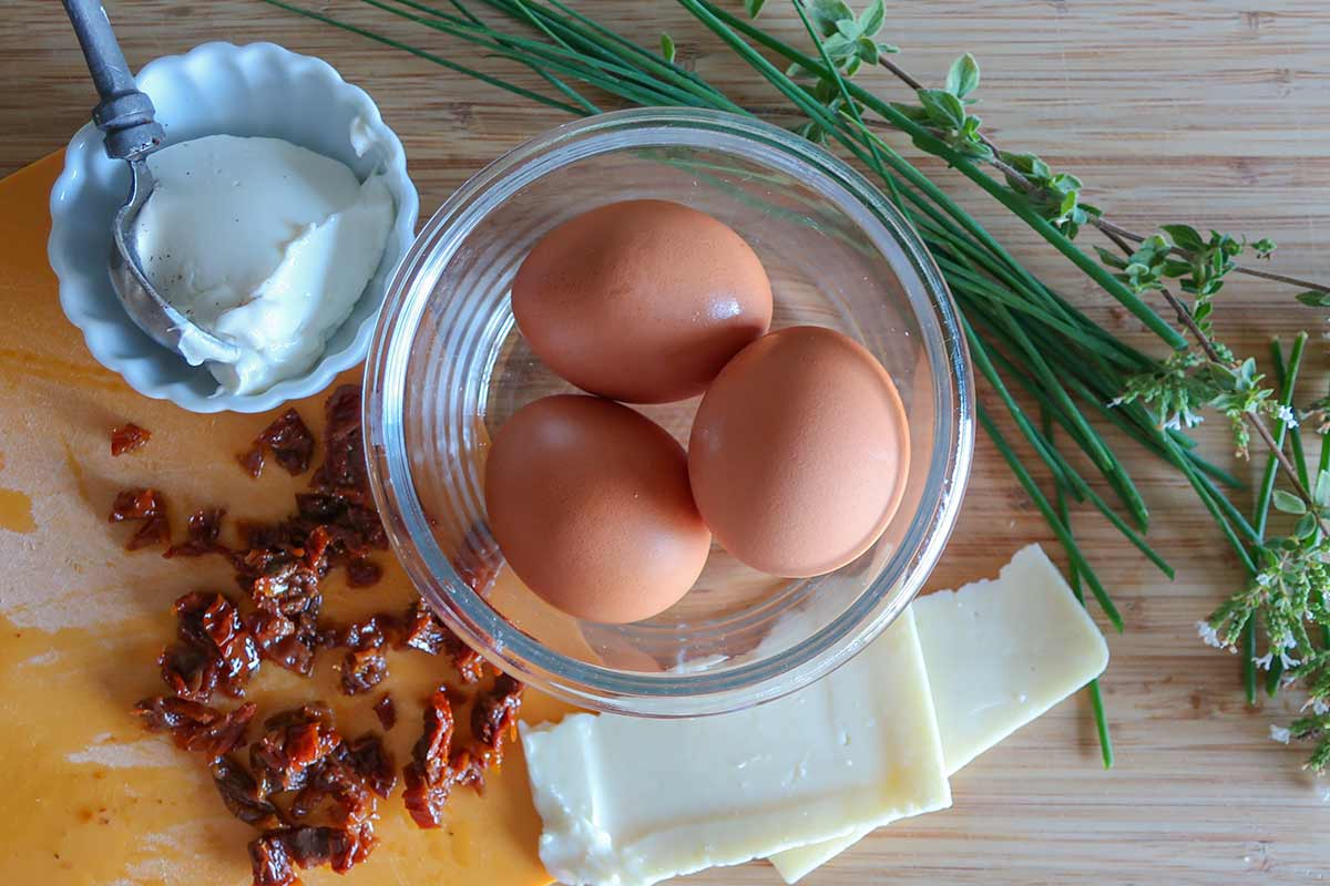 eggs, sour cream, chives, sun-dried tomatoes, cheese, and herbs on a cutting board