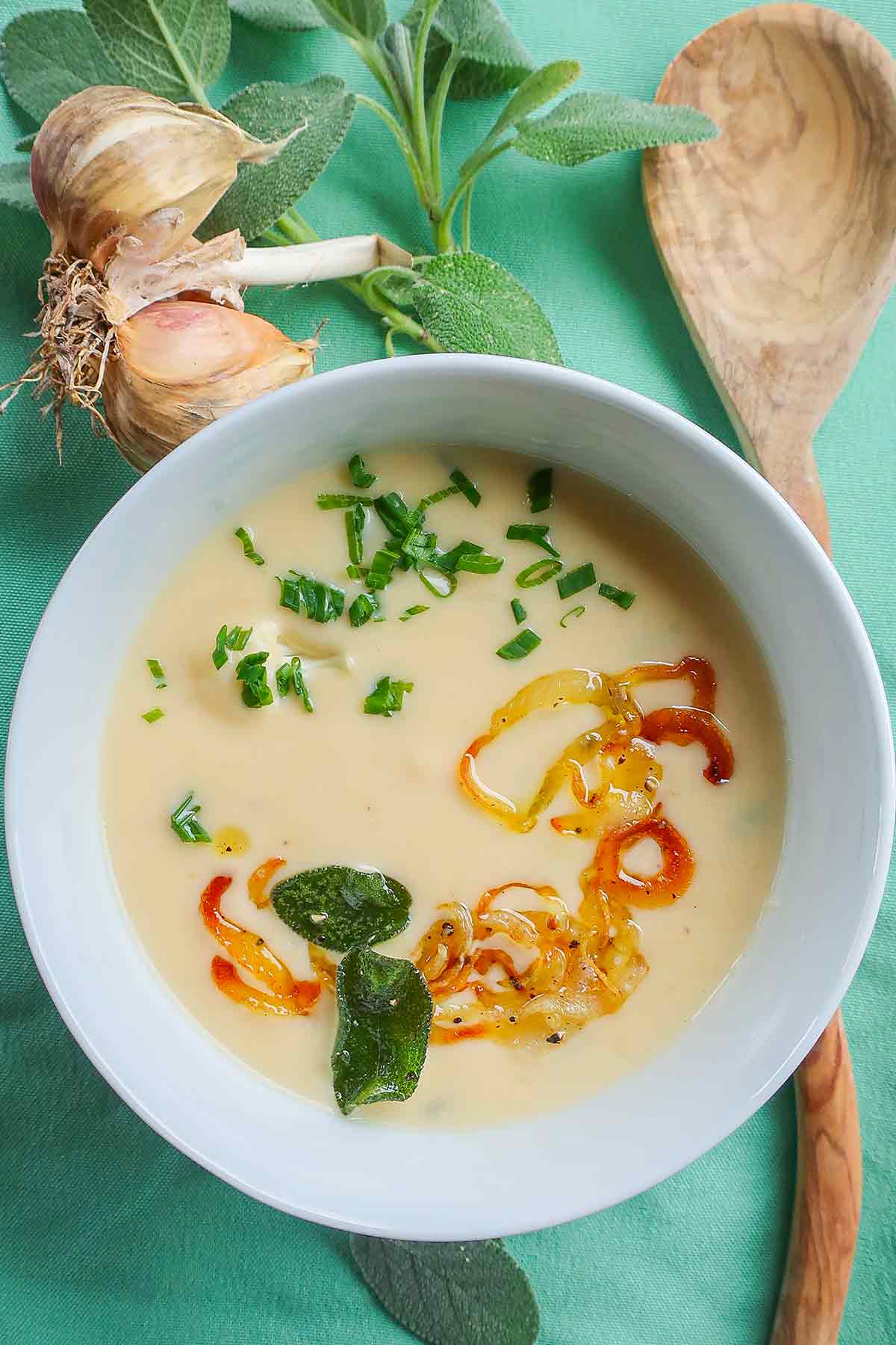 Cheesy Cauliflower Soup with Crispy Sage-Onion Topping with a wooden spoon on the side