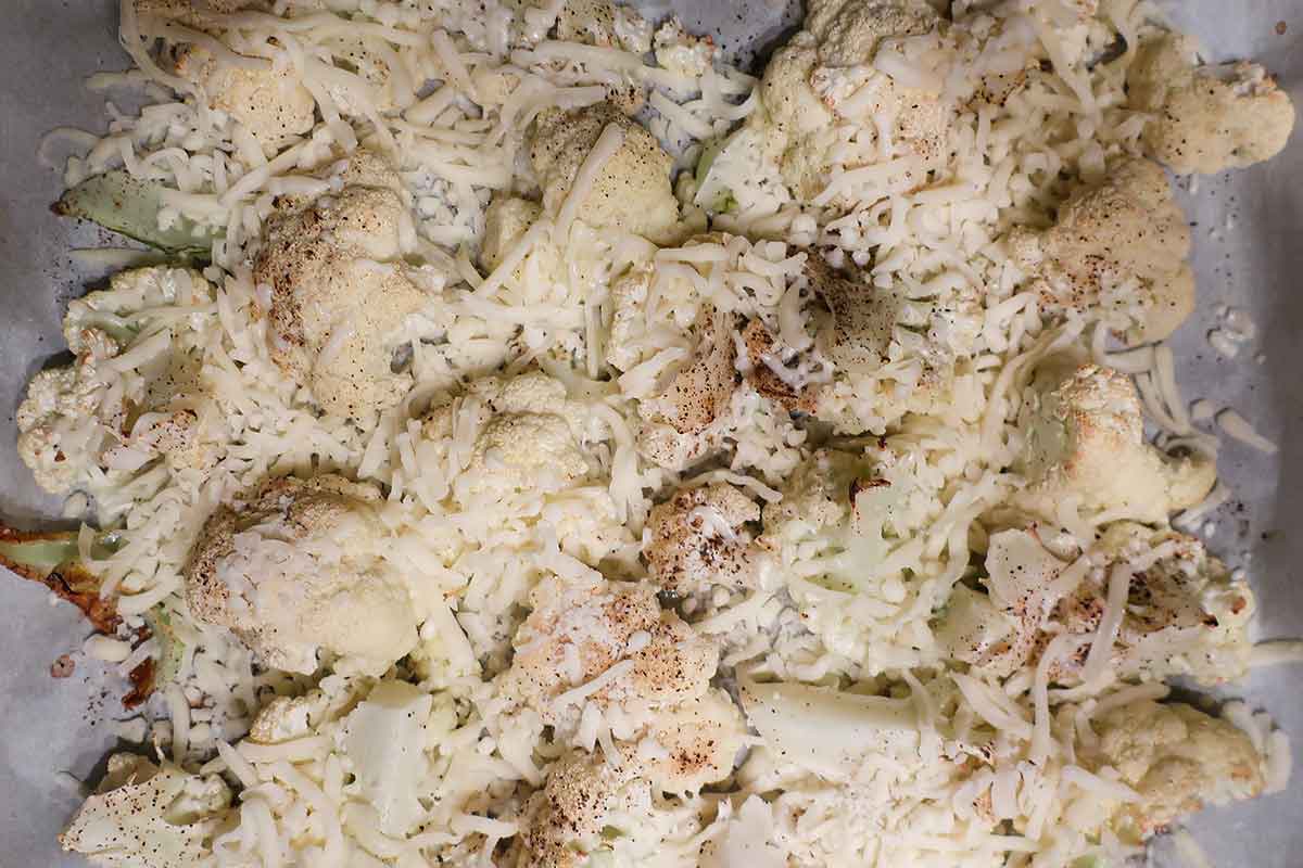 cauliflower on a baking sheet topped with shredded cheese before baking