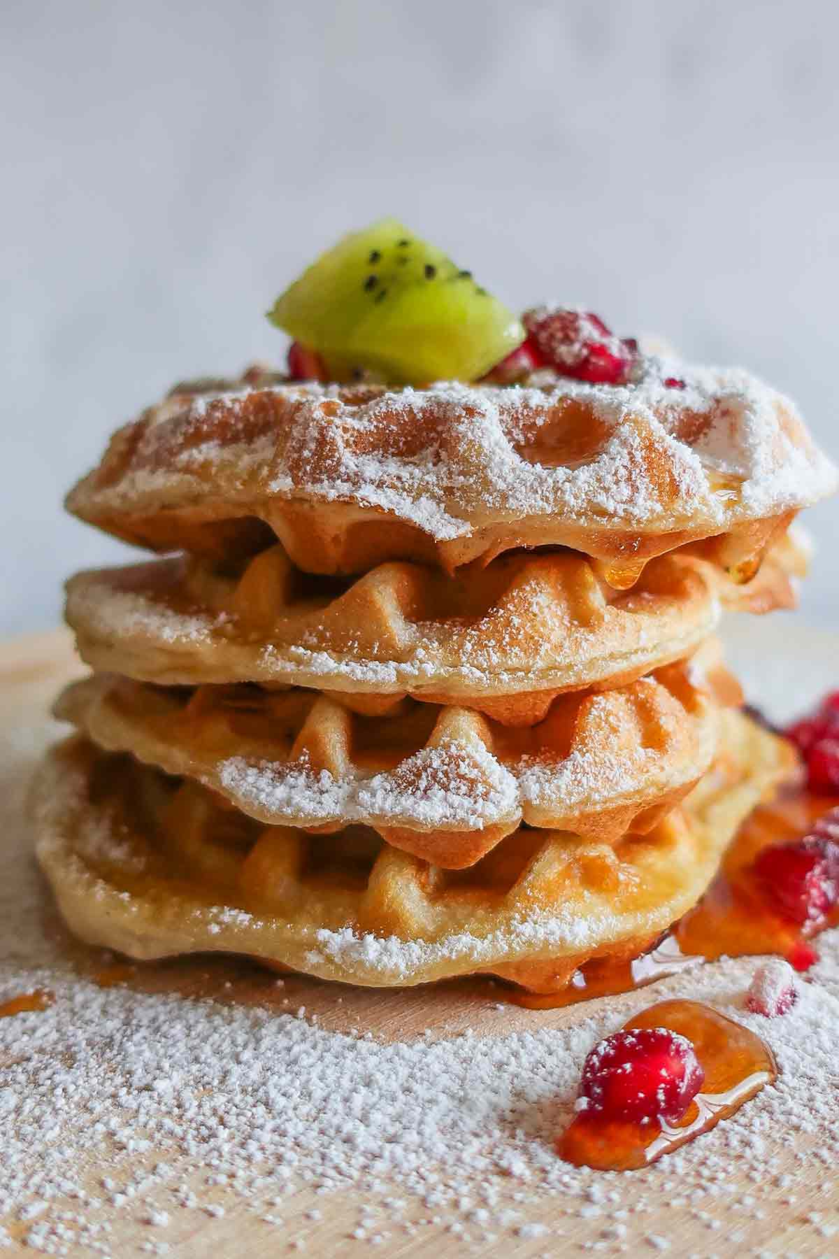 4 stacked gluten free waffles topped with kiwi and pomegranate seeds