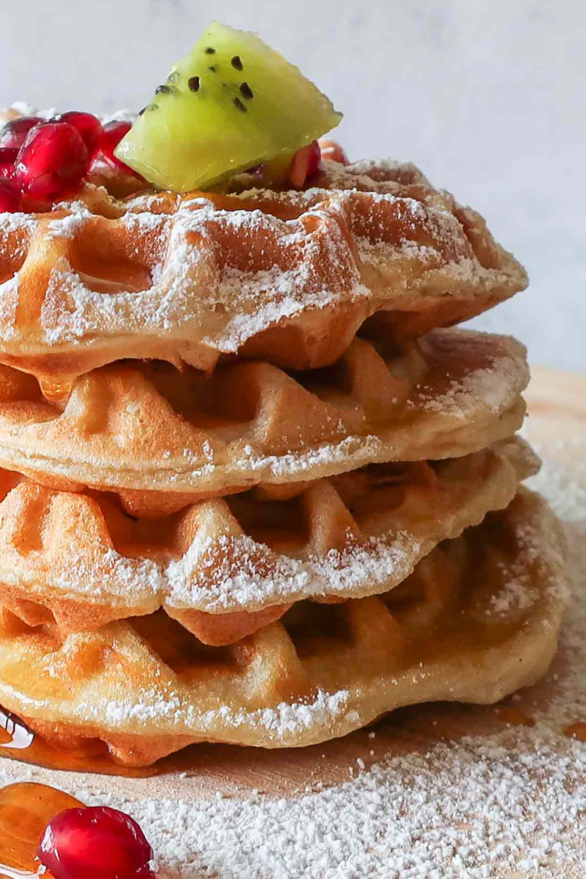 4 stacked gluten free waffles topped with fruit maple syrup and powdered sugar