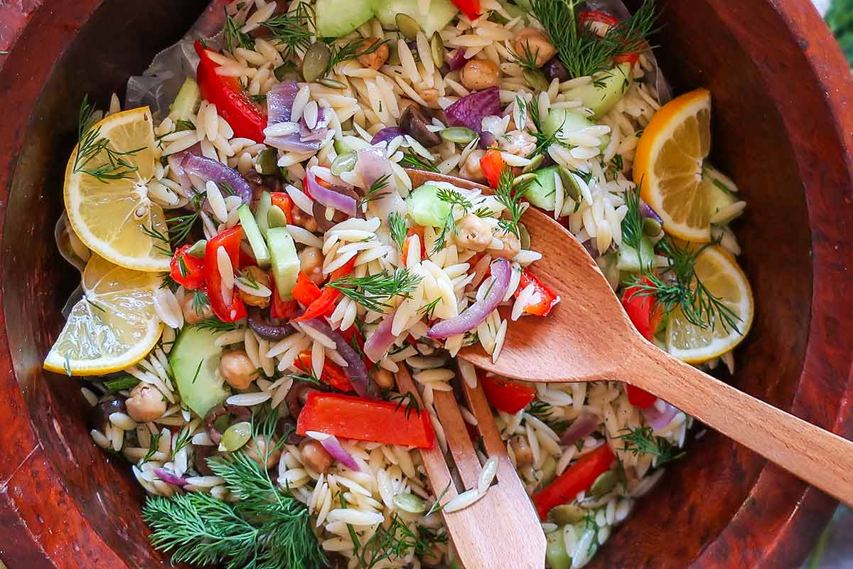 Orzo salad with fresh vegetables, served in a large wooden salad bowl