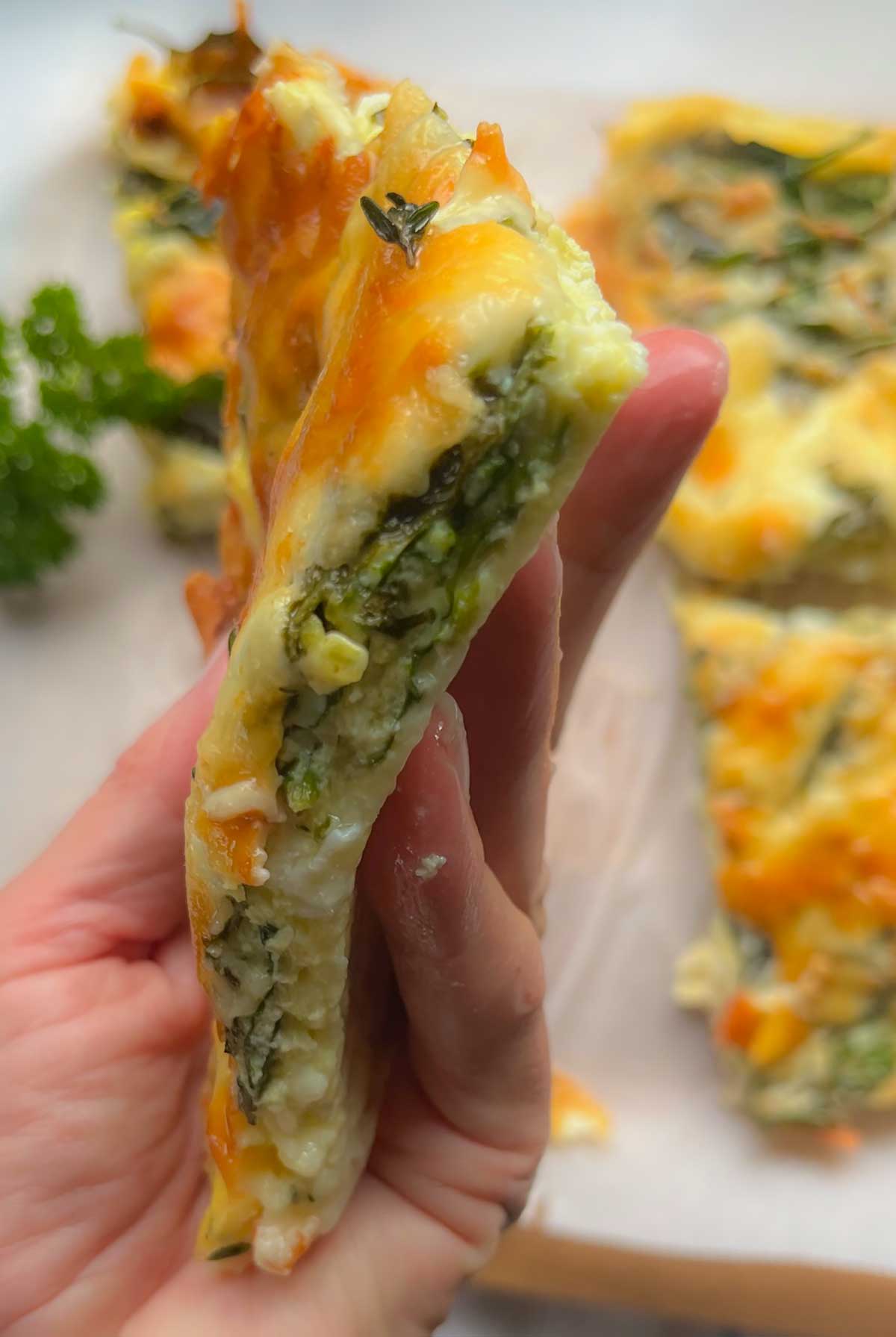 holding a slice of breakfast spinach and cheese quiche