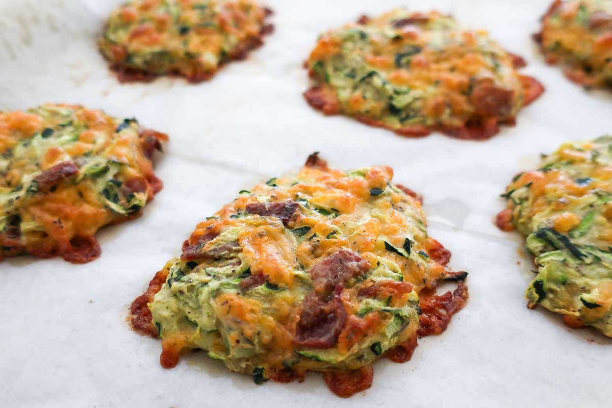 Close-up of freshly baked zucchini bites on a baking sheet, showing their golden, crispy edges and melted cheese.