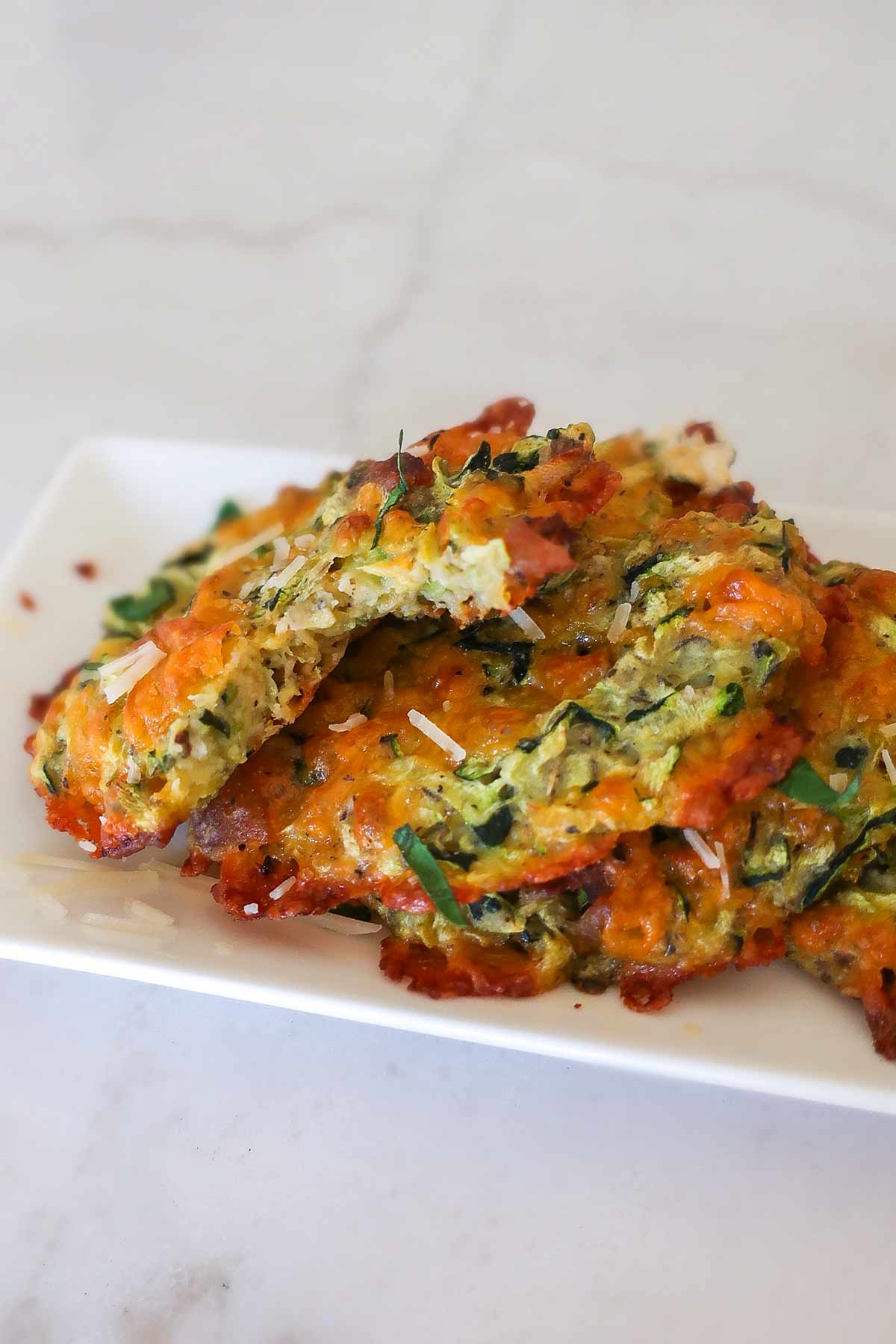 Close-up of golden-brown, gluten-free baked cheddar bacon zucchini bites arranged on a dessert plate, showcasing their crispy edges and cheesy texture.