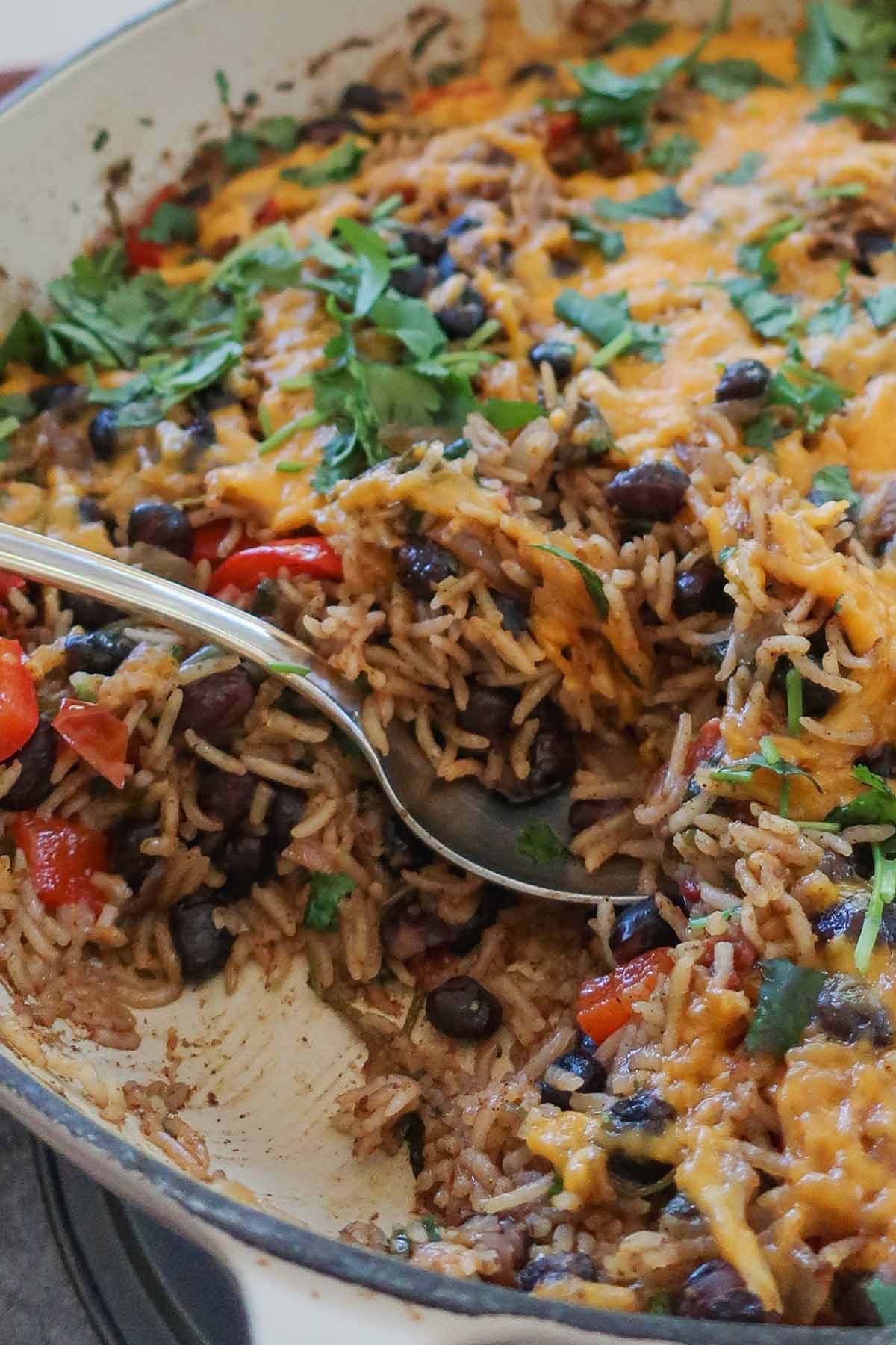 A close-up shot of a one-skillet no-tortilla veggie burrito on a spoon featuring melted cheddar cheese