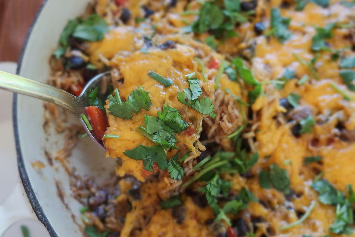 close up of skillet burrito bowl with black beans, veggies, rice, cheese and fresh cilantro on a spoon