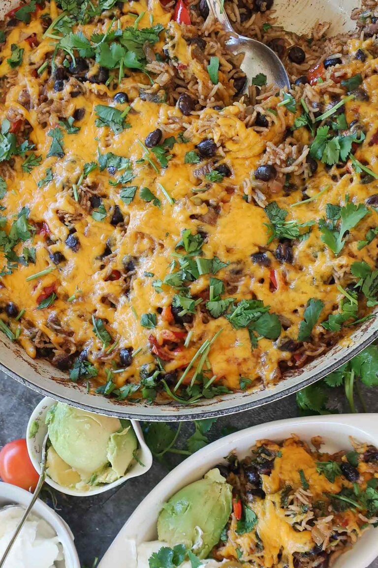A top-down photo of a gluten-free veggie burrito skillet filled with black beans, rice, and peppers, topped with melted cheddar cheese and fresh cilantro.