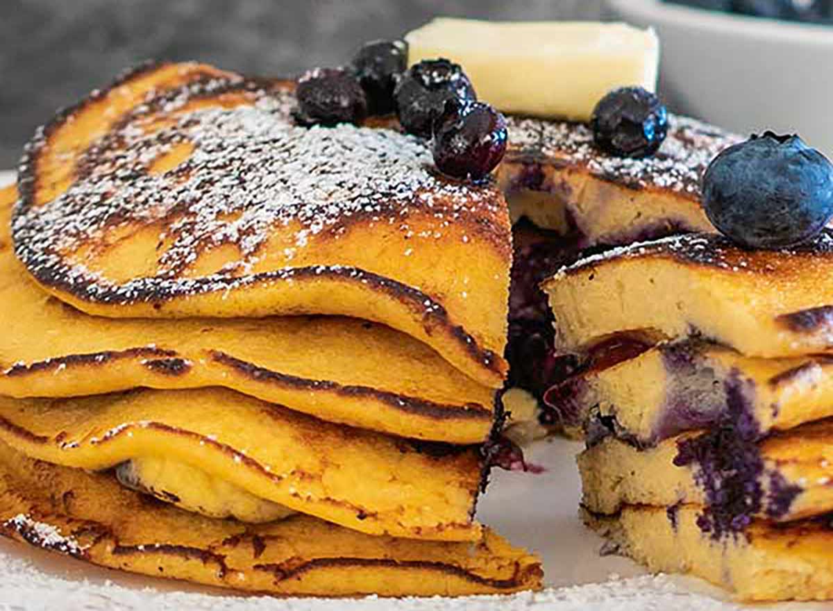 Coconut flour blueberry pancakes on a plate, topped with powdered sugar and cut open with a fork to reveal their fluffy, grain-free interior.