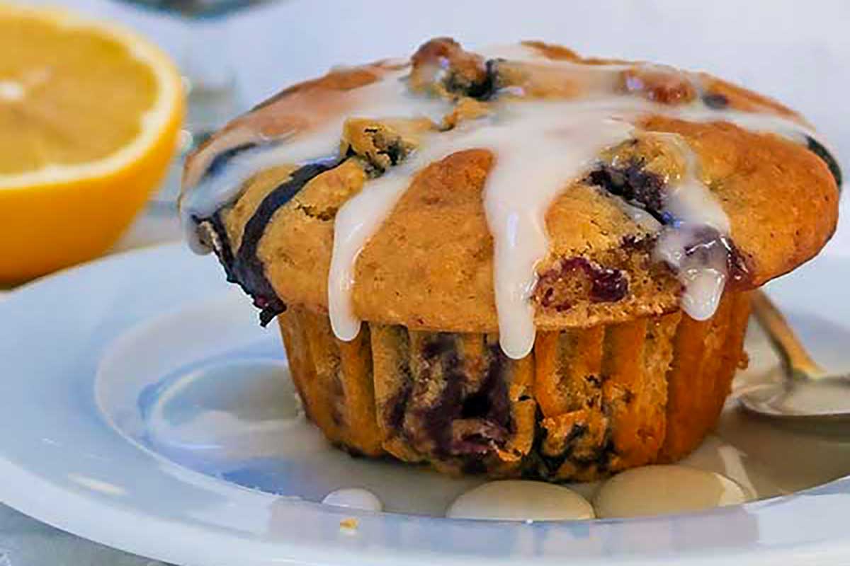 A light, fluffy muffin studded with juicy blueberries and drizzled with glossy lemon glaze, served on a plate—bright, fresh, and full of flavor
