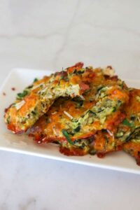 Close-up of golden-brown, gluten-free baked cheddar bacon zucchini bites arranged on a dessert plate, showcasing their crispy edges and cheesy texture.