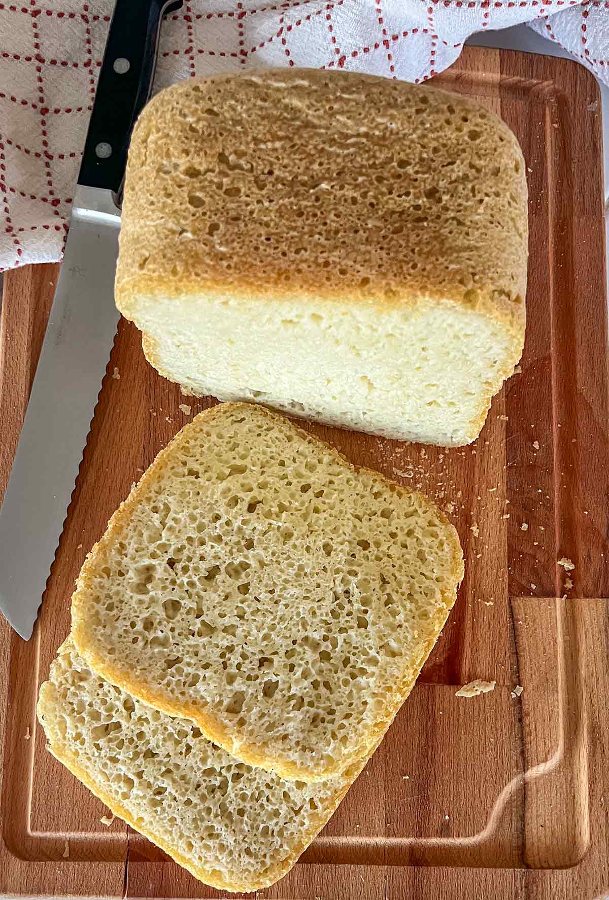 Whole loaf of gluten-free rice flour bread on a cutting board with 2 slices cut to show soft crumb and golden crust