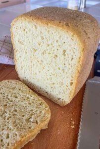 Whole loaf of gluten-free rice flour bread on a cutting board with one slice cut to show soft crumb and golden crust