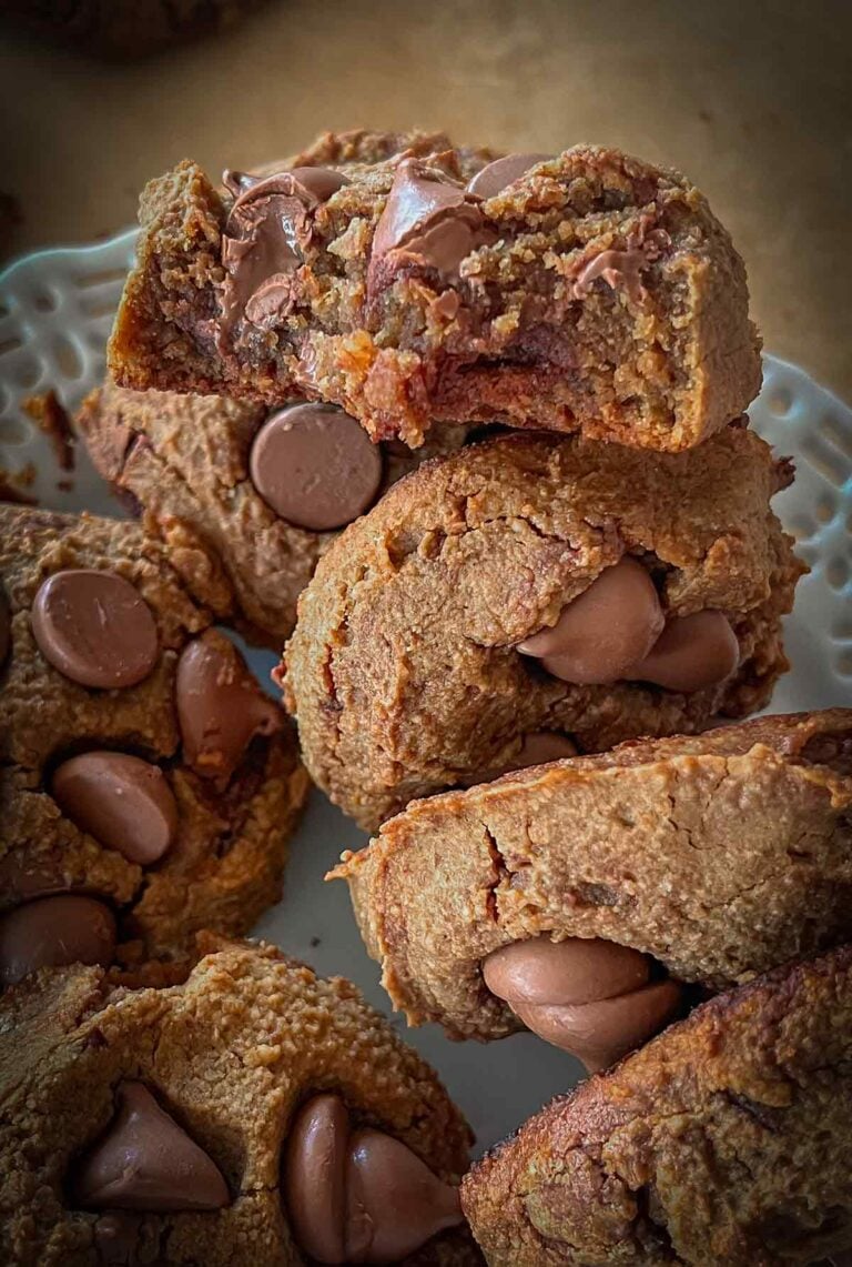 A plate of plant-based chocolate chickpea cookies, with one cookie broken in half to reveal a rich, fudgy interior texture.