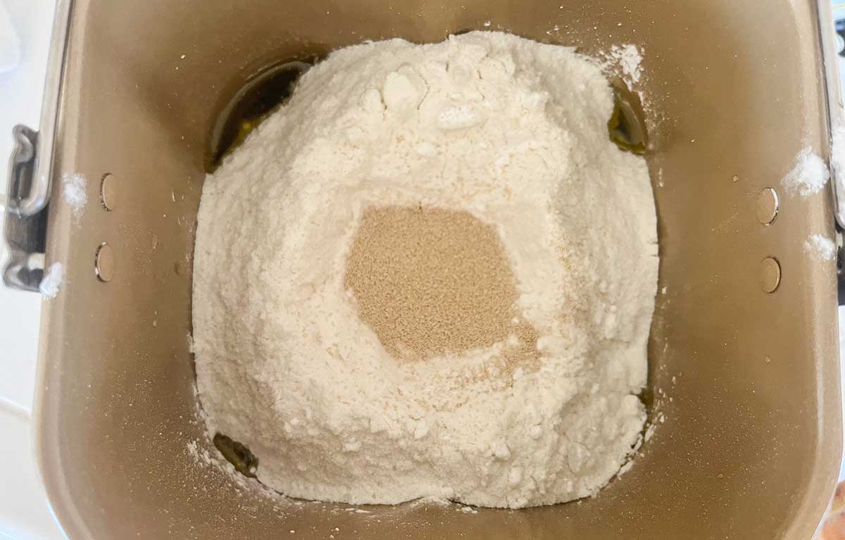 Dry ingredients layered on top of liquids in a bread machine pan with yeast sitting in a small well.