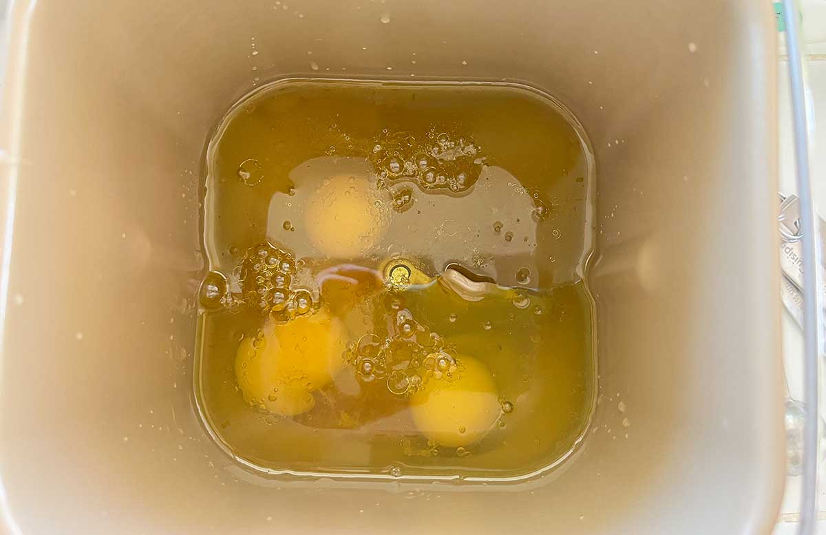 Bread machine pan with warm water, eggs, olive oil, and vinegar added first for gluten-free bread recipe.