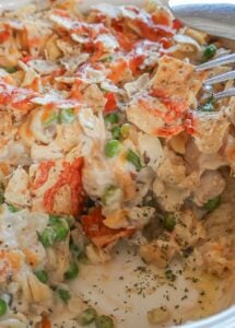 Baked gluten-free chicken noodle casserole in a deep ceramic casserole dish, showing creamy sauce, chunks of chicken, carrots, peas, and noodles; one slice is missing, revealing the soft, cheesy interior.