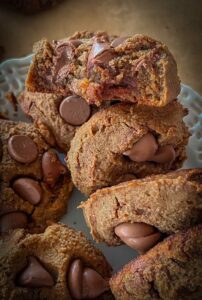 A plate of plant-based chocolate chickpea cookies, with one cookie broken in half to reveal a rich, fudgy interior texture.