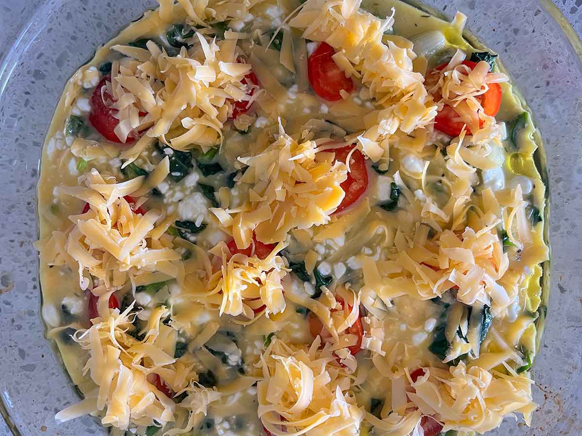 assembled spinach and cottage cheese topped with sliced tomatoes and cheese in a pan before baking