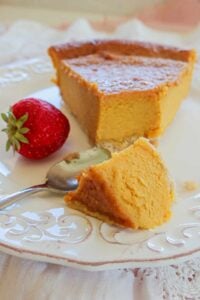 Close-up of a slice of gluten-free vanilla pumpkin pie on a plate, showing creamy filling and golden almond crust.