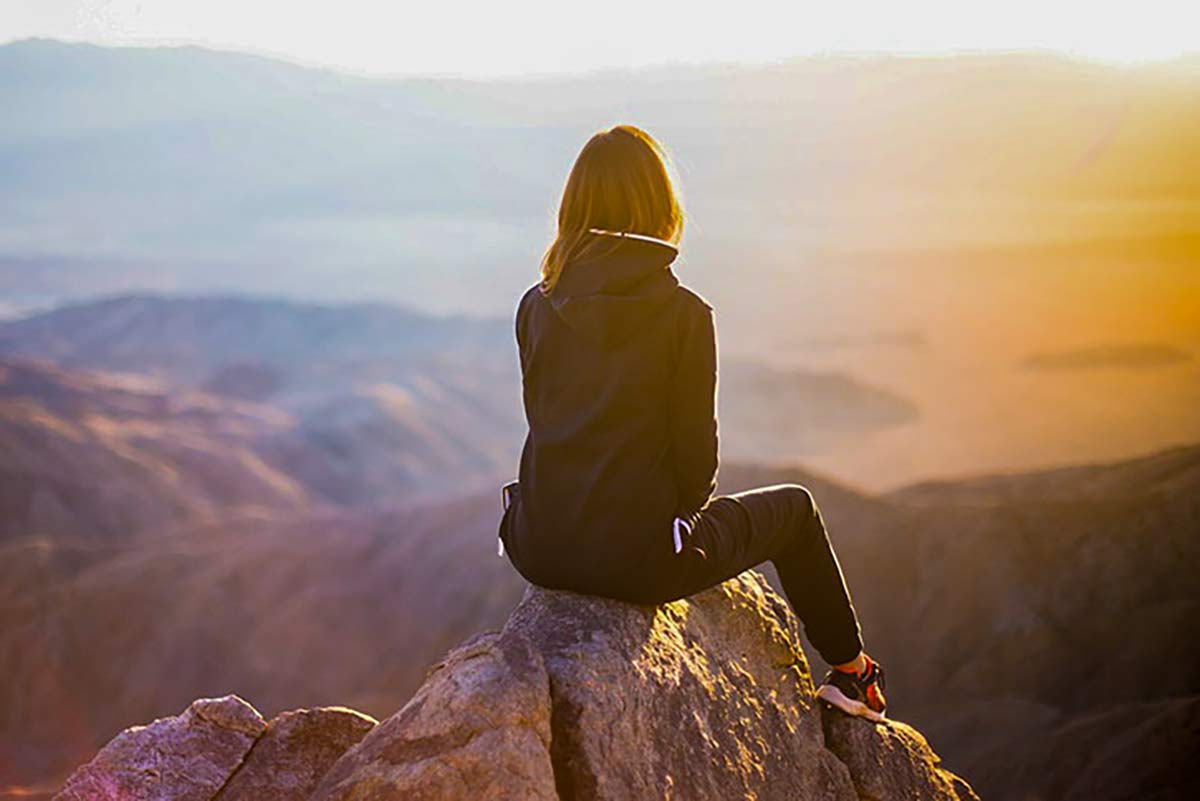 woman sitting on top of a mountain on a rock and thinking