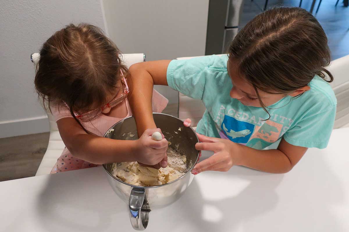 Two kids mixing dough together in a stand mixer while baking Crumbl-style gluten-free sugar cookies.